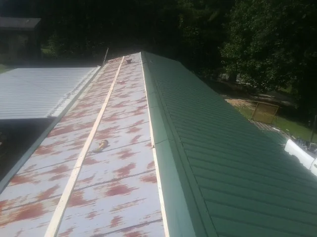Old rusted panels beside newly installed green metal roofing — Wind Damage Roof Repair by Roofing Brothers in Luke Air Force Base