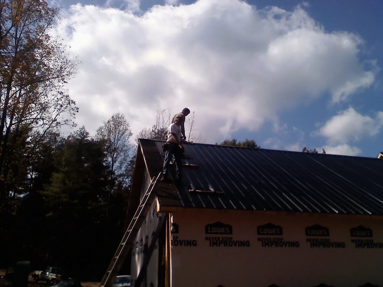 Roofer fastening dark metal panels high against a cloudy sky, from a Roof Inspection job in Luke Air Force Base