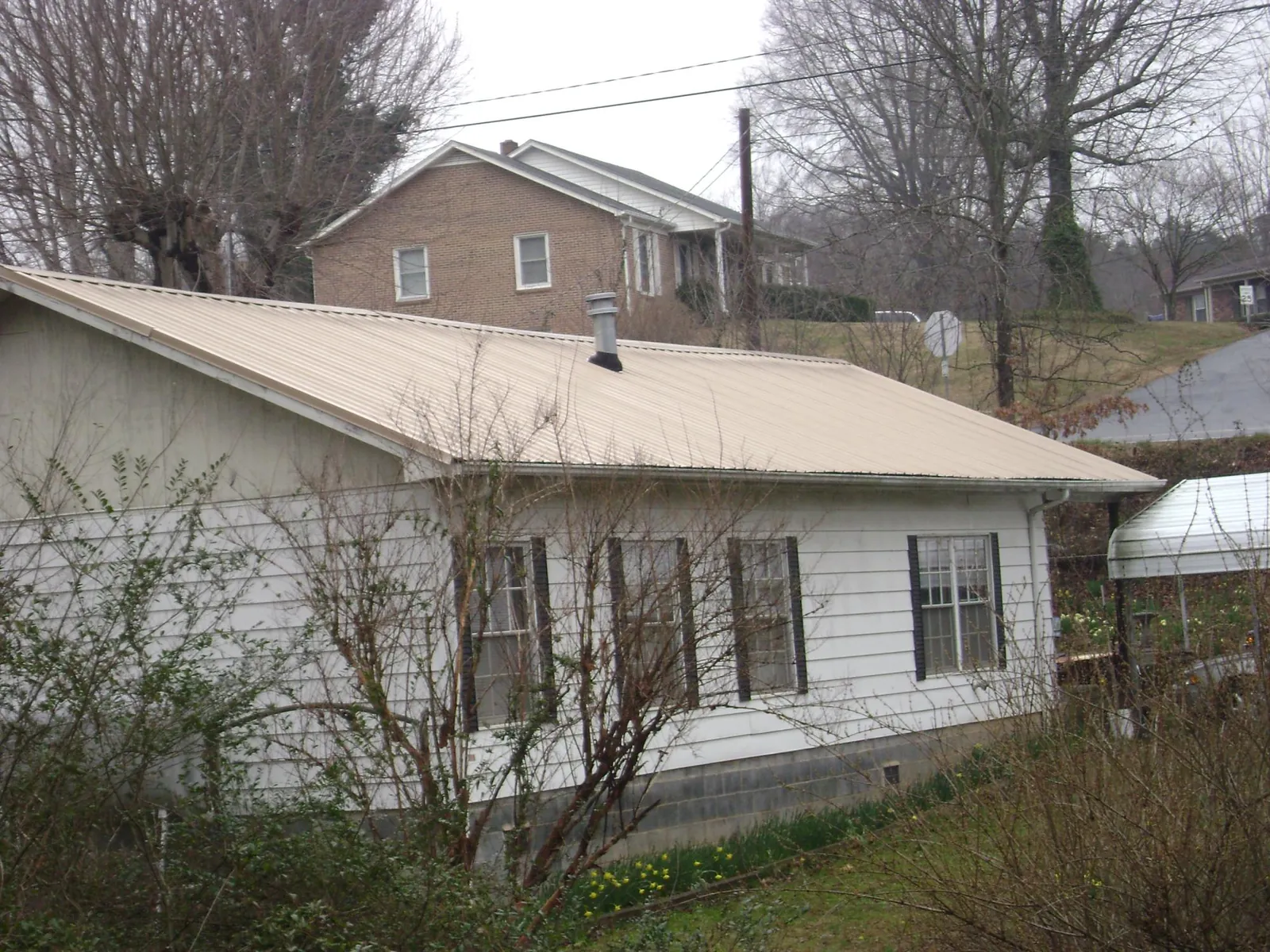 Tan metal roof on a white sided house set into a hillside — Commercial Roofing by Roofing Brothers in Luke Air Force Base